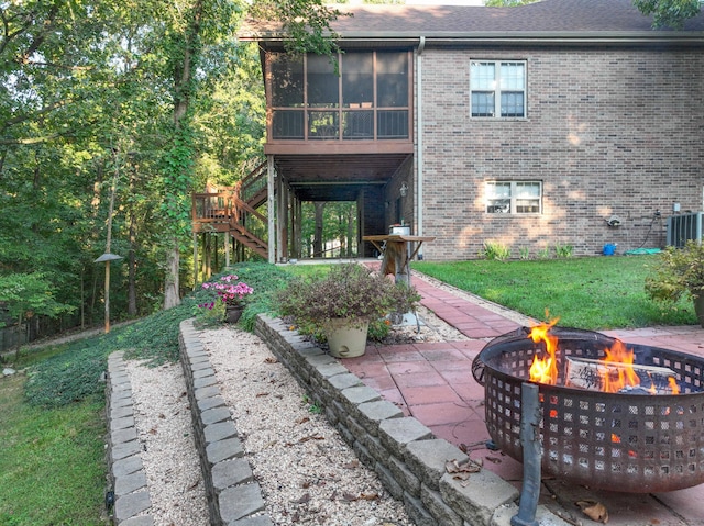 back of house featuring a fire pit, a sunroom, a lawn, central AC unit, and a patio