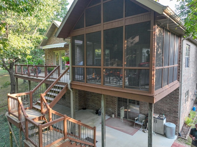 back of property featuring a wooden deck, a sunroom, and a patio