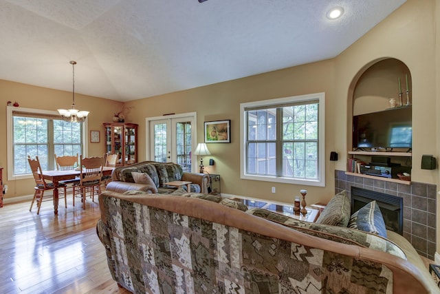 living room featuring lofted ceiling, light wood-type flooring, a textured ceiling, a fireplace, and a notable chandelier