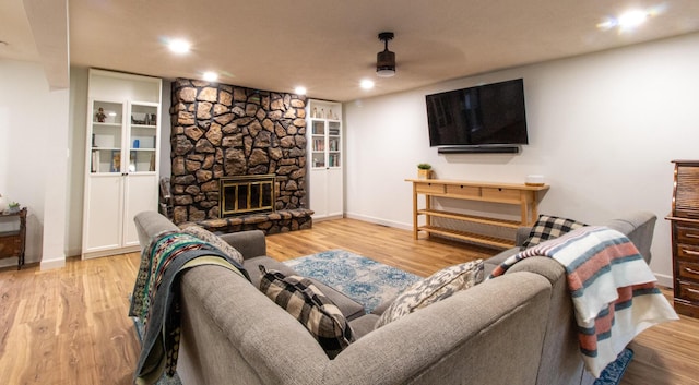 living room featuring ceiling fan, a stone fireplace, built in features, and light hardwood / wood-style flooring