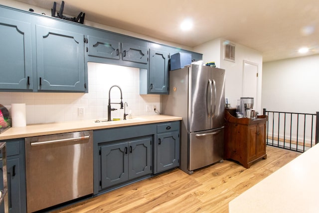 kitchen featuring backsplash, sink, light wood-type flooring, blue cabinetry, and appliances with stainless steel finishes