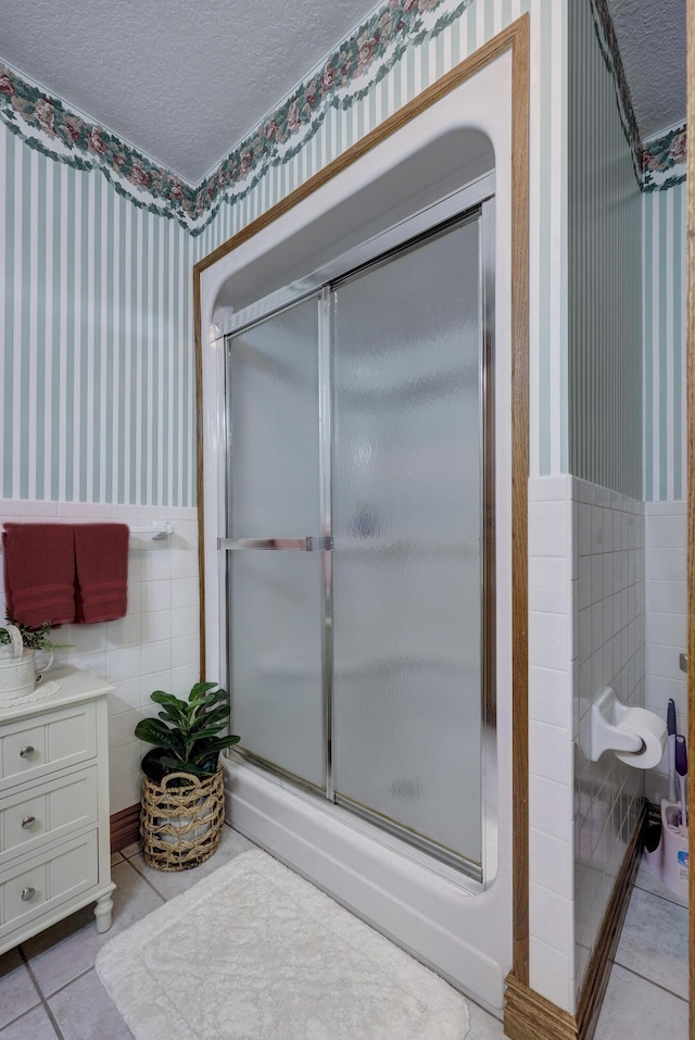 bathroom with tile patterned flooring, a textured ceiling, tile walls, and a shower with shower door