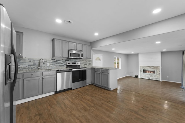 kitchen featuring kitchen peninsula, appliances with stainless steel finishes, gray cabinetry, sink, and a fireplace