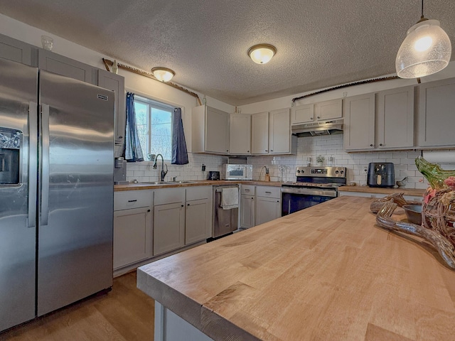 kitchen featuring pendant lighting, sink, stainless steel appliances, and wooden counters