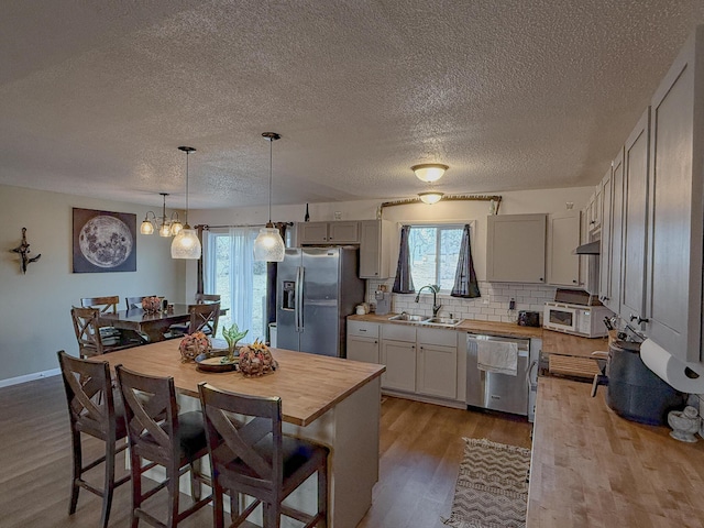 kitchen with a kitchen island, stainless steel appliances, hanging light fixtures, and wooden counters
