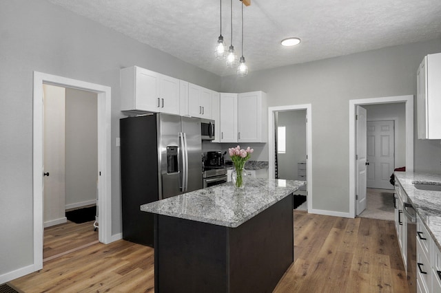 kitchen with light stone countertops, white cabinetry, a center island, stainless steel appliances, and pendant lighting