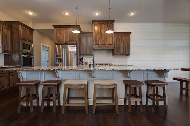 kitchen featuring light stone counters, an island with sink, hanging light fixtures, and appliances with stainless steel finishes