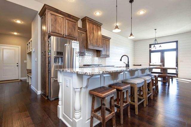 kitchen featuring hanging light fixtures, high end fridge, light stone counters, a breakfast bar, and a center island with sink