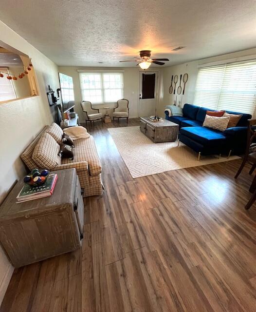 living room featuring wood-type flooring, a textured ceiling, and ceiling fan