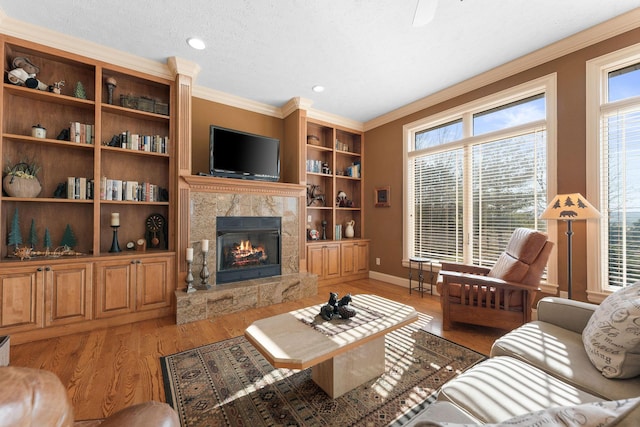 living room featuring a wealth of natural light, light hardwood / wood-style flooring, crown molding, and a stone fireplace