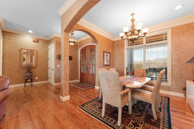 dining area with french doors, an inviting chandelier, ornamental molding, and light hardwood / wood-style flooring