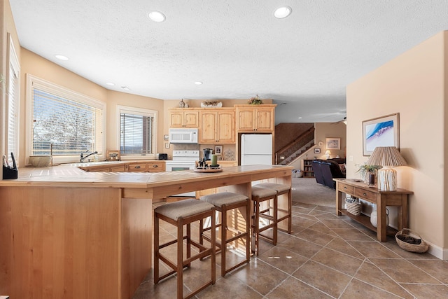 kitchen with a kitchen breakfast bar, a textured ceiling, kitchen peninsula, and white appliances