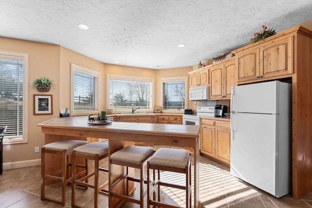 kitchen featuring tile countertops, a wealth of natural light, white appliances, and a breakfast bar area