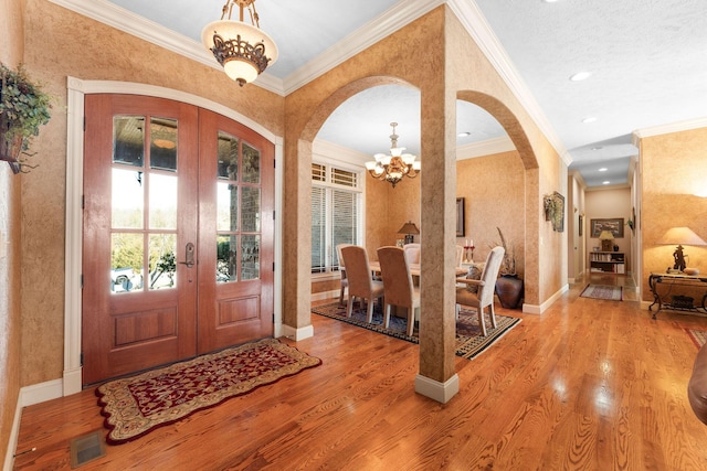 foyer featuring light wood-type flooring, a chandelier, french doors, a textured ceiling, and ornamental molding