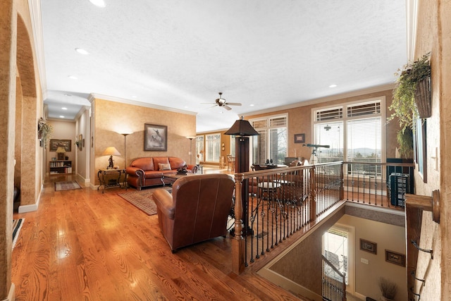 living room featuring hardwood / wood-style flooring, a textured ceiling, ornamental molding, and ceiling fan