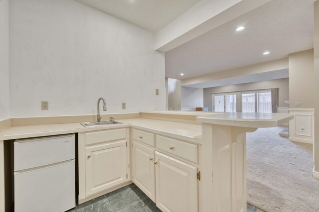 kitchen featuring sink, kitchen peninsula, refrigerator, a breakfast bar area, and dark carpet