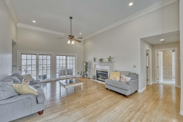 living room featuring ceiling fan, light hardwood / wood-style flooring, a high ceiling, and ornamental molding