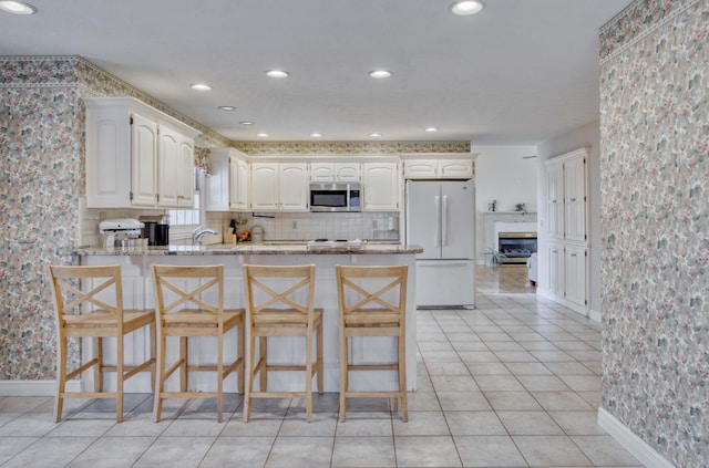 kitchen featuring a kitchen breakfast bar, kitchen peninsula, white fridge, light stone counters, and white cabinetry