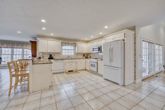 kitchen with light stone countertops, white appliances, white cabinetry, and a wealth of natural light