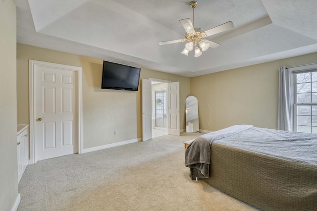 bedroom featuring multiple windows, light carpet, a raised ceiling, and ceiling fan