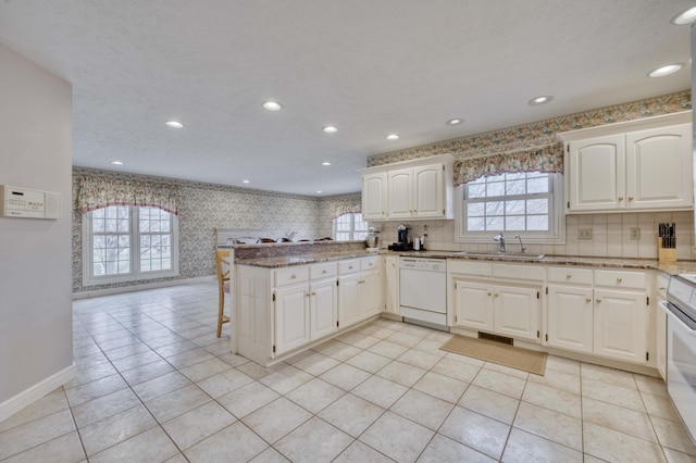 kitchen featuring white cabinetry, sink, light stone countertops, kitchen peninsula, and white dishwasher