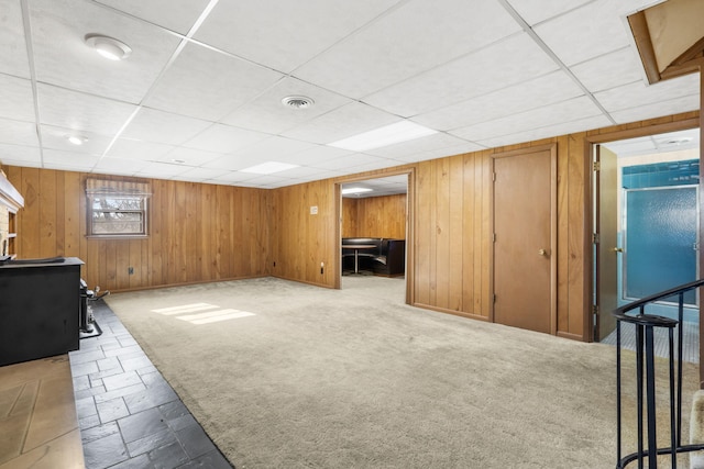 basement with carpet flooring, a paneled ceiling, and wooden walls