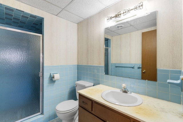 bathroom featuring walk in shower, a drop ceiling, vanity, tile walls, and toilet