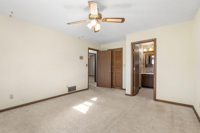 unfurnished bedroom with ceiling fan, a closet, light carpet, and ensuite bath