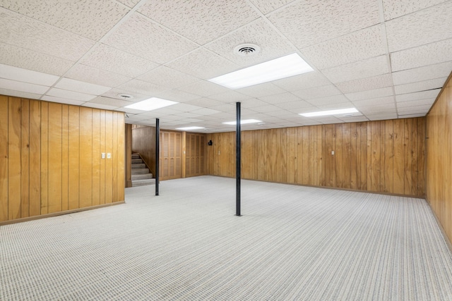 basement featuring a drop ceiling and wooden walls