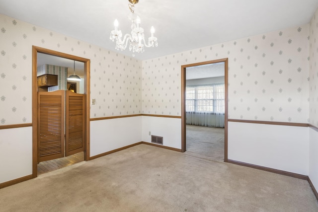 carpeted spare room with an inviting chandelier