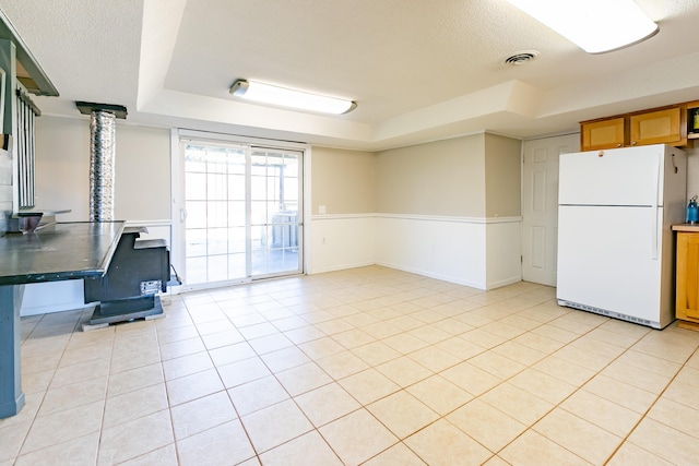 kitchen featuring visible vents, freestanding refrigerator, light tile patterned flooring, a textured ceiling, and a raised ceiling