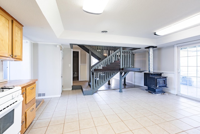 kitchen featuring visible vents, baseboards, white gas stove, light tile patterned floors, and a wood stove