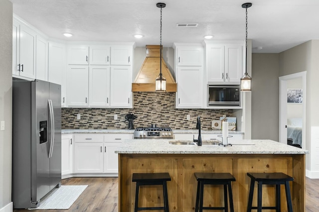 kitchen featuring an island with sink, premium range hood, appliances with stainless steel finishes, and tasteful backsplash