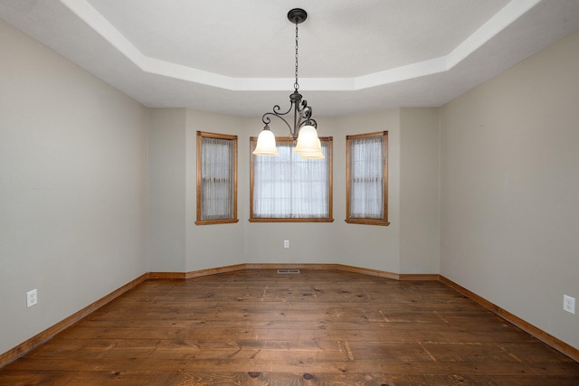 empty room featuring dark hardwood / wood-style floors, a raised ceiling, and an inviting chandelier