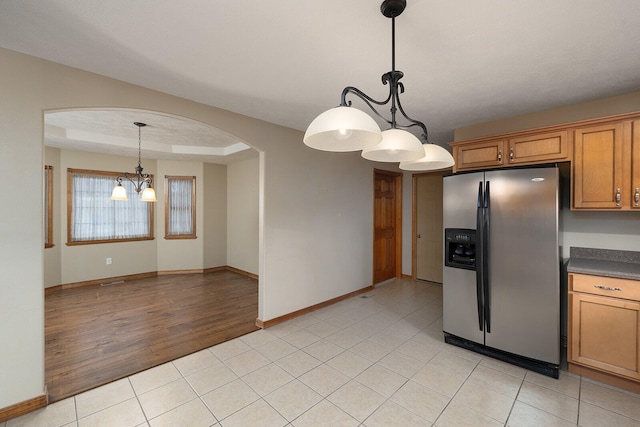 kitchen with an inviting chandelier, a raised ceiling, hanging light fixtures, light tile patterned floors, and stainless steel fridge with ice dispenser