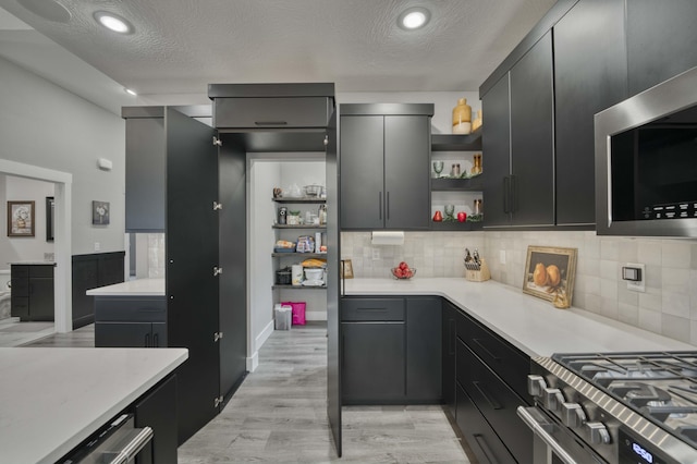 kitchen with a textured ceiling, decorative backsplash, light hardwood / wood-style floors, and stainless steel appliances