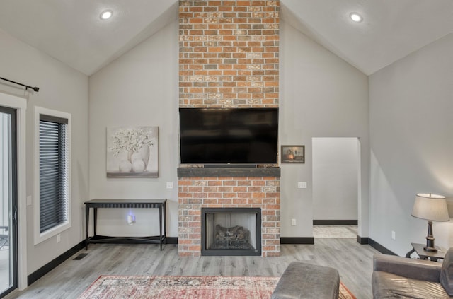 living room featuring a brick fireplace, high vaulted ceiling, and light hardwood / wood-style flooring