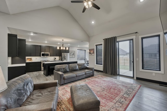 living room with ceiling fan with notable chandelier, light hardwood / wood-style floors, and high vaulted ceiling