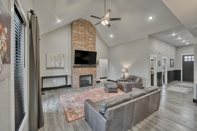 living room with a brick fireplace, ceiling fan, high vaulted ceiling, and light wood-type flooring