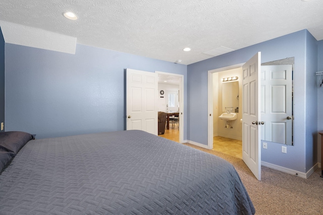 bedroom featuring ensuite bath, light colored carpet, and a textured ceiling