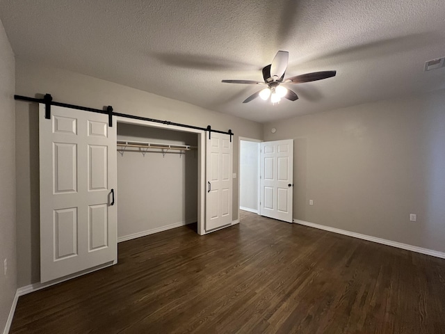 unfurnished bedroom with ceiling fan, a barn door, dark hardwood / wood-style flooring, a textured ceiling, and a closet