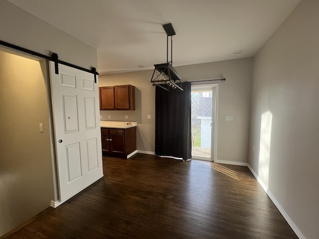 unfurnished dining area featuring a barn door and dark wood-type flooring