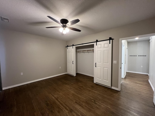 unfurnished bedroom featuring dark wood-type flooring, ceiling fan, a barn door, a textured ceiling, and a closet