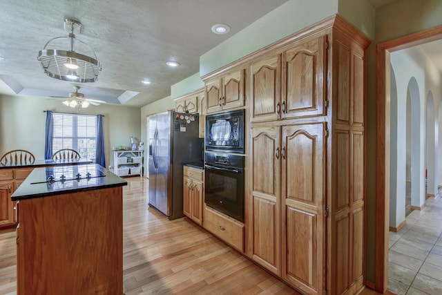 kitchen featuring ceiling fan, light hardwood / wood-style floors, black appliances, a kitchen island, and a textured ceiling