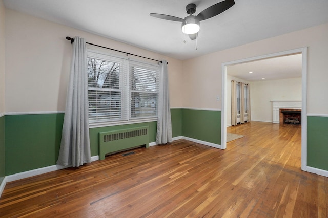 spare room featuring ceiling fan, radiator heating unit, and wood-type flooring