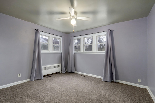 carpeted spare room with a wealth of natural light, radiator, and ceiling fan