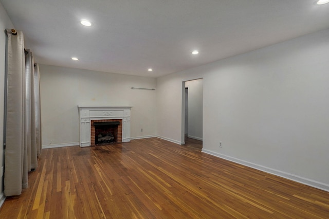 unfurnished living room with wood-type flooring and a brick fireplace