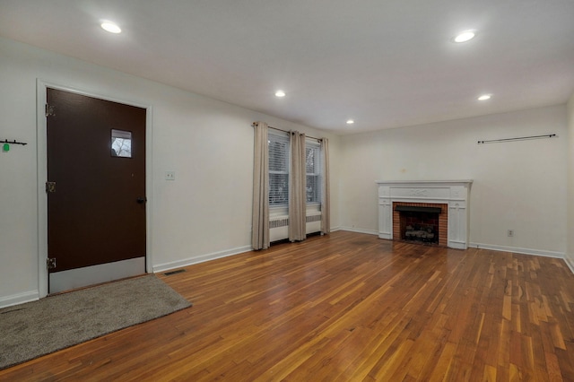 unfurnished living room with wood-type flooring and a brick fireplace