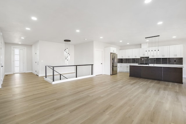 kitchen featuring white cabinetry, backsplash, stainless steel fridge, pendant lighting, and a kitchen island