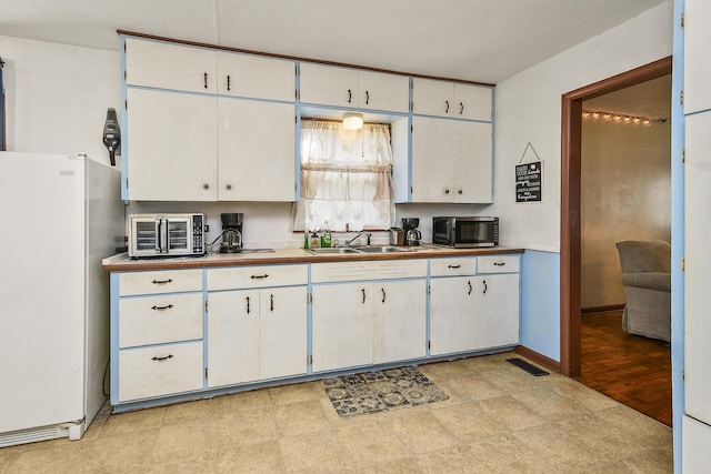 kitchen with white cabinets, sink, and white fridge